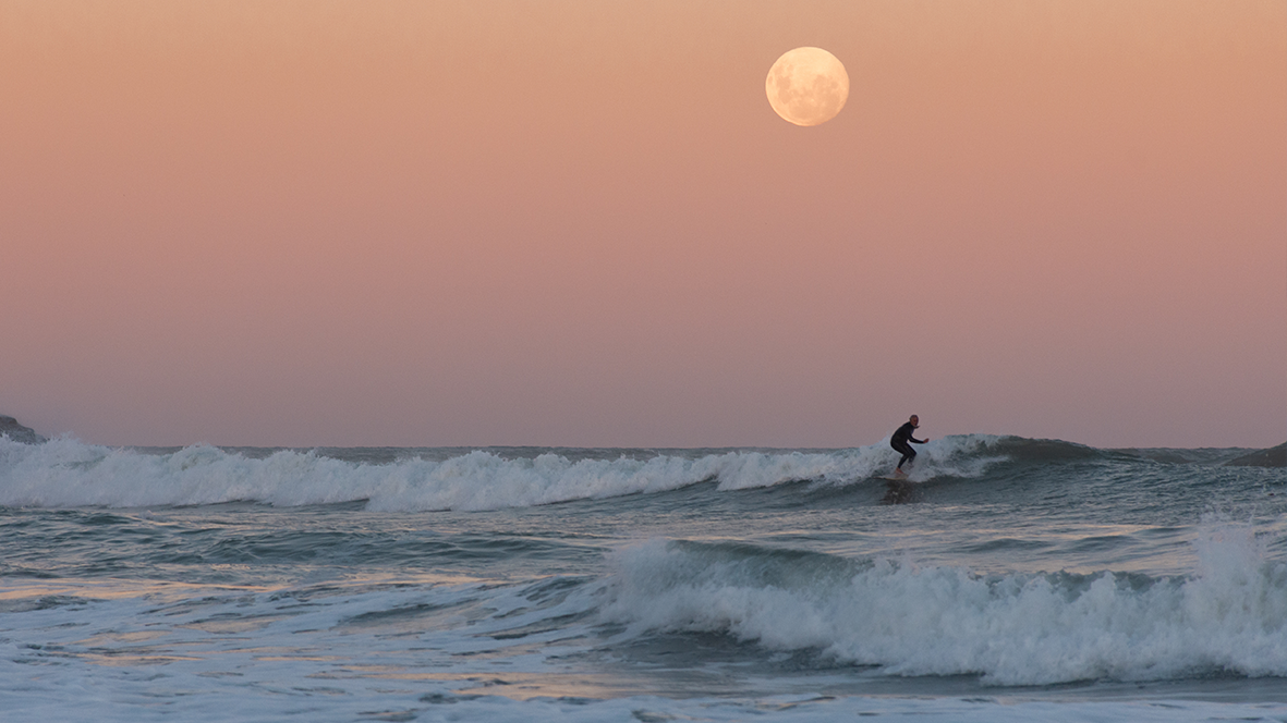 Photographie d'un surfeur au coucher du soleil en phase de pleine lune